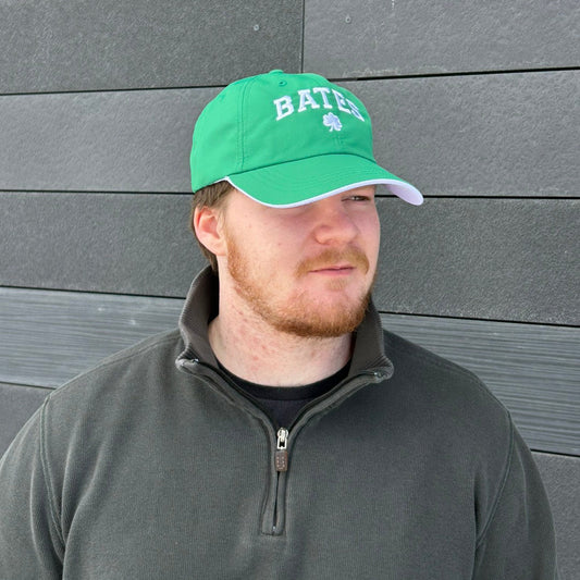 Man wearing a green cap with 'Bates' logo against a gray wooden wall