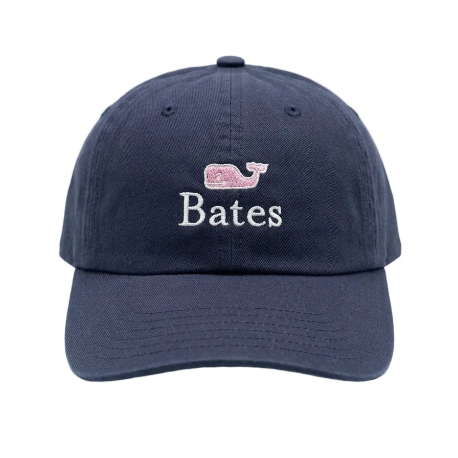 A navy blue baseball cap with an embroidered pink whale logo and the name 'Bates' in white on the front, set against a clean white background.