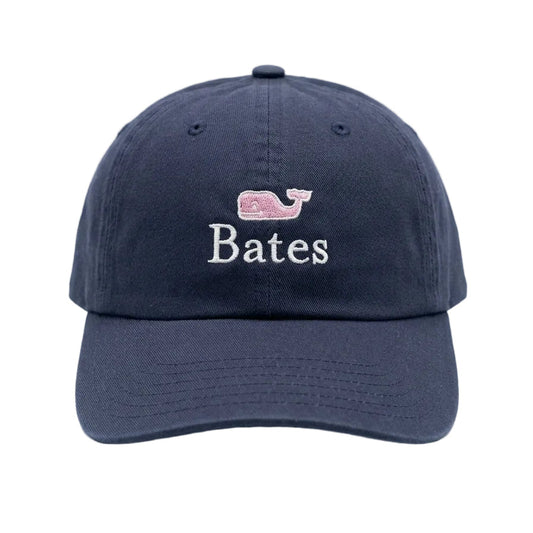 A navy blue baseball cap with an embroidered pink whale logo and the name 'Bates' in white on the front, set against a clean white background.